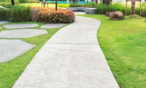 Concrete Walkway Across a Lawn With Bushes And Garden